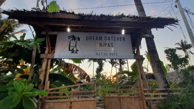 A bamboo entrance with a sign reading Dream Catcher Nipas Native Huts, surrounded by tropical plants in Siargao.