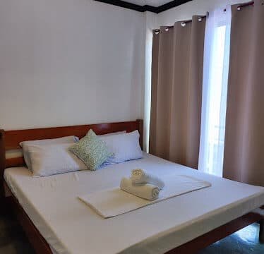 A neatly made bed with pillows and towels near a window with beige curtains, evoking the relaxed vibe of Siargao in a bright room.