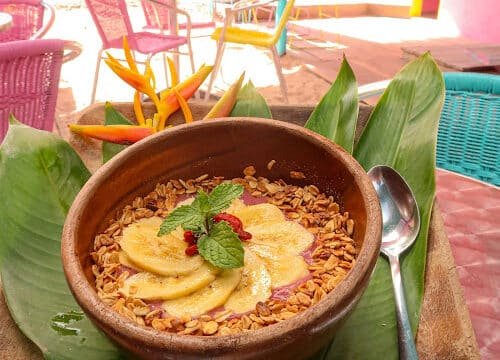 A smoothie bowl topped with banana slices, granola, and mint, served on banana leaves—perfect for a Siargao-inspired breakfast.