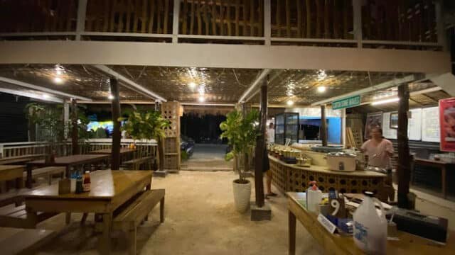 Open-air restaurant in Siargao with wooden tables, lush plants, and a counter, all warmly lit in the evening.