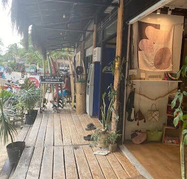 Wooden boardwalk with potted plants, shop displays, and a Little Italy Entrance sign creates a Siargao-inspired ambiance.