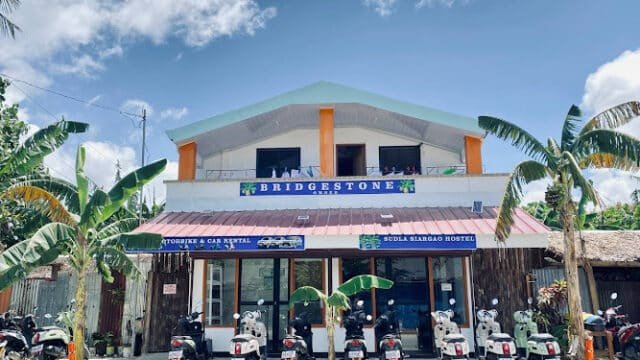 Two-story building with a Bridgestone sign in Siargao, scooters parked out front, and palm trees under a blue sky.