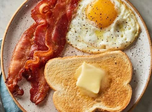 Plate with two strips of bacon, a sunny-side-up egg, and toast topped with butter, inspired by Siargao mornings.
