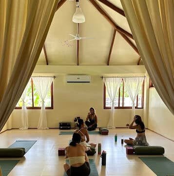 Four people practice yoga on mats in a bright, airy Siargao studio with large windows and wooden beams.