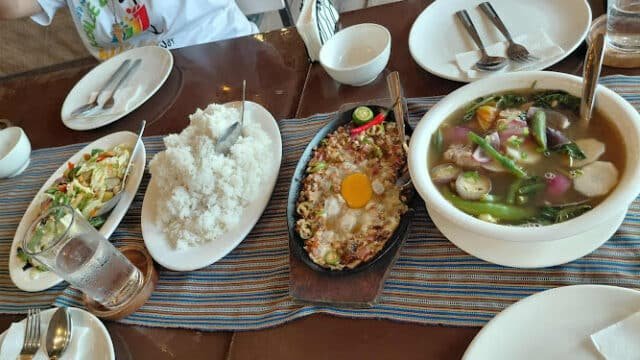 A table with rice, soup, stir-fried vegetables, and a sizzling dish awaits, bringing a taste of Siargao to your meal.