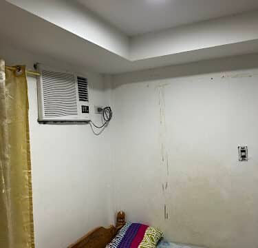 A small Siargao bedroom with a bed, pillows, wall air conditioner, and a light on the ceiling.