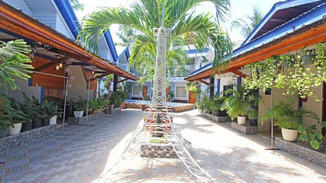 Courtyard with potted plants, palm tree, and Siargao-style tropical buildings on both sides under a sunny sky.