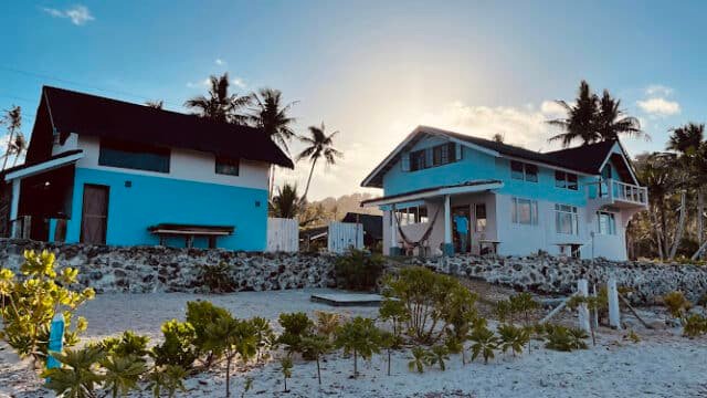 Two blue beach houses with palm trees on the sandy Siargao shore at sunset.