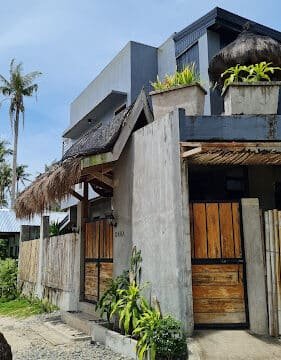 Modern Siargao house with wooden gates, concrete walls, and tropical plants under a clear blue sky.