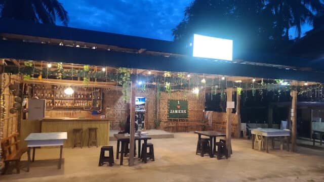 Outdoor bar in Siargao with string lights, wooden tables and stools, lush plants, and a tropical evening sky in the background.