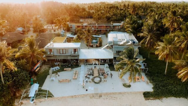 Aerial view of a beachside resort in Siargao with palm trees and outdoor seating near the shoreline at sunset.