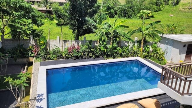 Rectangular outdoor pool surrounded by lush greenery and a wooden deck, evoking the tropical vibe of Siargao.