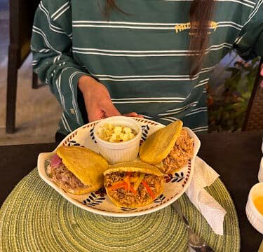 Person holding a plate with three stuffed arepas and a small bowl of salad on a green placemat in Siargao.