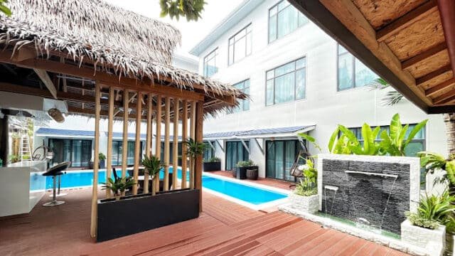 Outdoor pool area with a thatched-roof cabana, modern fountain, tropical plants, and Siargao-inspired lounge seating.