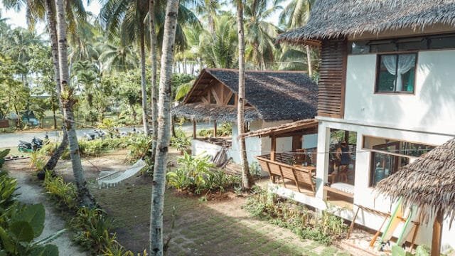 Tropical garden in Siargao with palm trees, hammocks, and thatched-roof houses basking under bright sunlight.