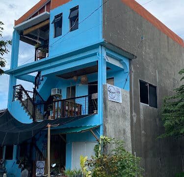 A three-story blue building in Siargao with a cafe sign, outdoor seating, and lush plants in front.