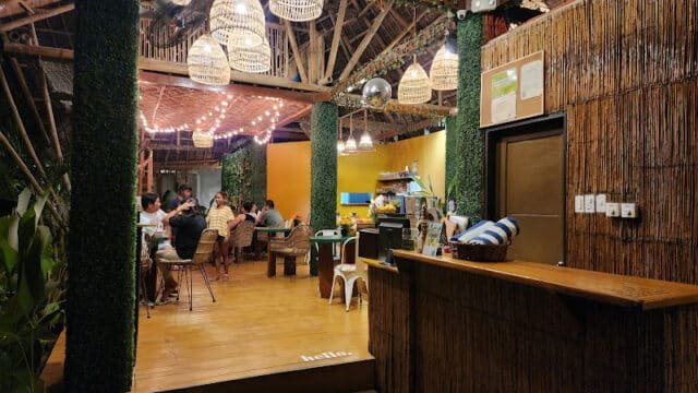 A cozy, bamboo-themed café in Siargao with people dining and warm string lights hanging from the ceiling.