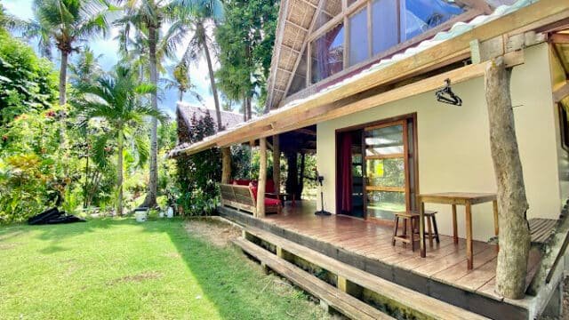 A tropical wooden house with a porch, surrounded by lush green trees and bright Siargao sunlight.