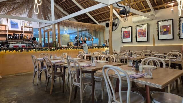 Casual Siargao restaurant with wooden tables, art on walls, open kitchen, and tropical, thatched roof decor.