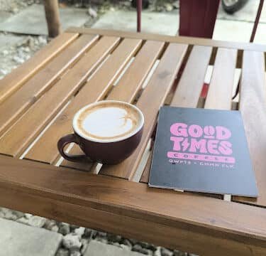 A cup of coffee and a menu sit on a wooden table at an outdoor café in sunny Siargao.