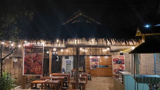 A rustic open-air restaurant in Siargao at night, lit by string lights, with wooden tables and a dog lying on the ground.