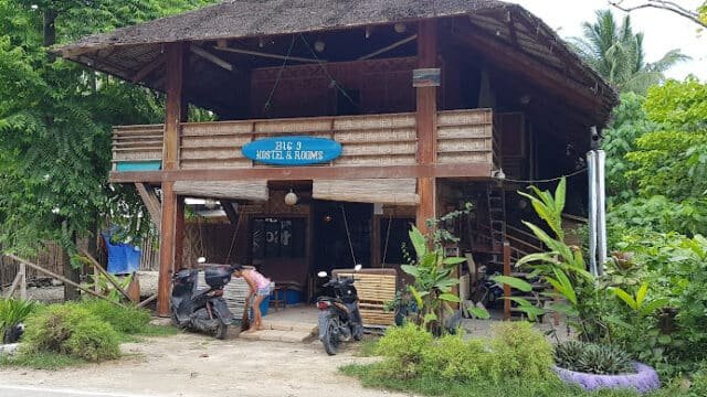 A rustic wooden hostel in Siargao with motorbikes parked outside, surrounded by lush greenery and tropical plants.