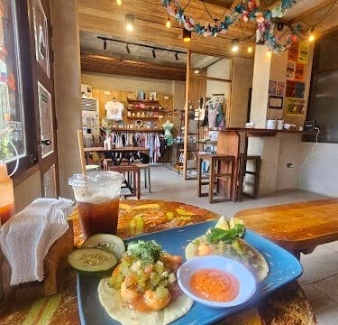 Plate of tacos with sauces and iced drink on a colorful table in a cozy, rustic Siargao cafe with clothes in the background.