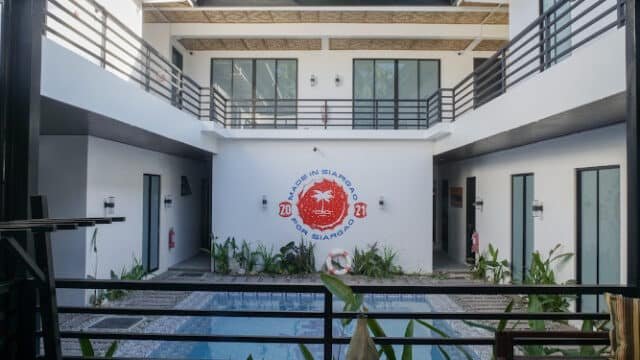 Modern two-story building in Siargao with rooms around a small pool and lush plants, all viewed from a balcony.
