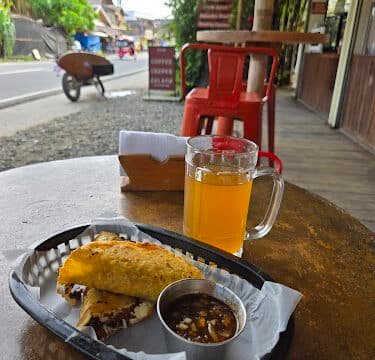 A sandwich and dip with a glass of iced tea on a table at an outdoor café by the roadside in Siargao.