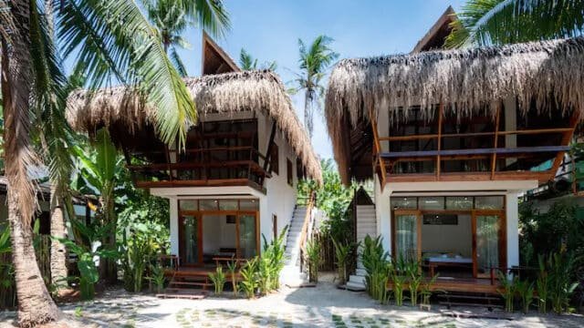 Two tropical bungalows with thatched roofs and balconies nestle among palm trees under Siargao’s bright blue sky.