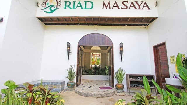 Entrance to Riad Masaya in Siargao with plants, lanterns, and a white sign above a wooden door.