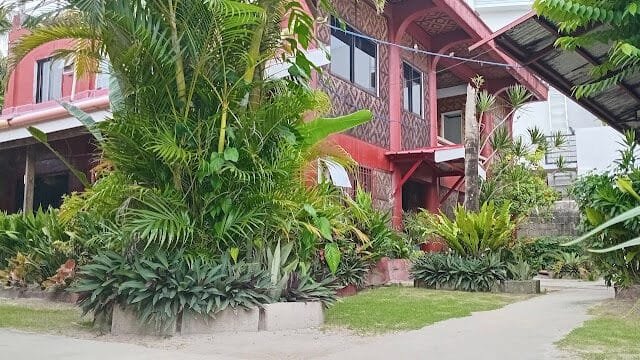 Red house in Siargao with lush tropical plants and greenery surrounding the entrance and pathways.