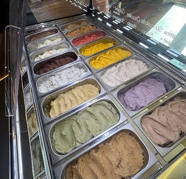 A display case filled with colorful gelato flavors in metal trays at a cozy Siargao ice cream shop.