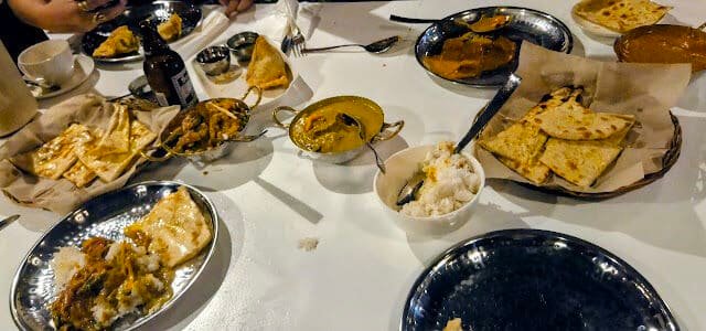 Plates of Indian food, naan, curry, and drinks on a white table in Siargao, with people dining together.