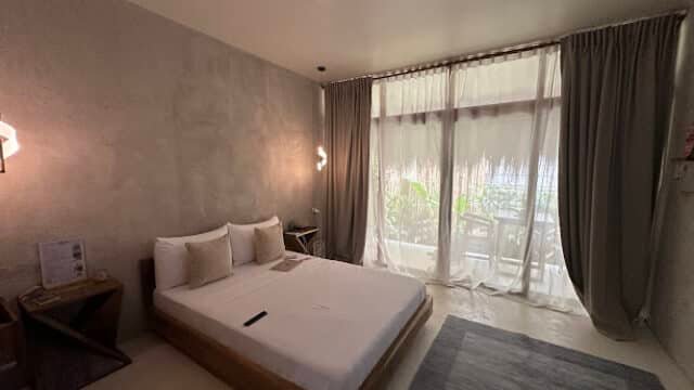Minimalist bedroom with a double bed, large window with curtains, and a tranquil Siargao view of lush greenery outside.