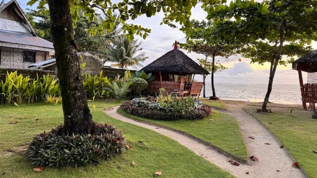 Curved sandy paths lead to huts by the beach in Siargao, surrounded by trees and greenery, with the ocean in the background.