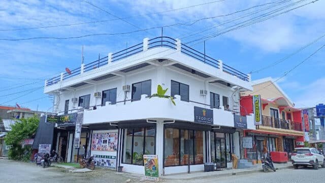 Two-story white building with balconies, shops on the ground floor, under Siargao’s bright blue sky.