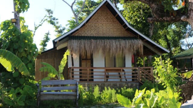 A small tropical hut with a thatched roof and wooden porch, surrounded by lush green plants, inspired by Siargao’s island charm.