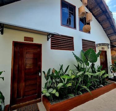 A tropical Siargao guesthouse with wooden doors, lush green plants, and woven lanterns under a thatched roof.