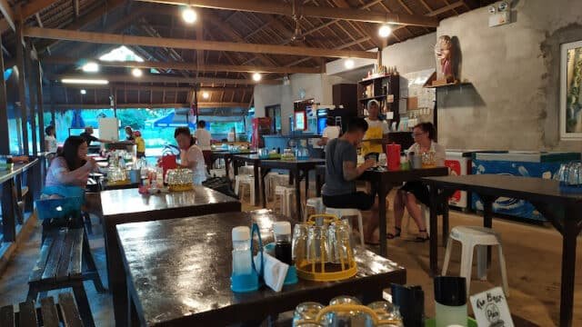 Open-air Siargao restaurant with wooden tables, people dining, and a rustic atmosphere under a thatched roof.