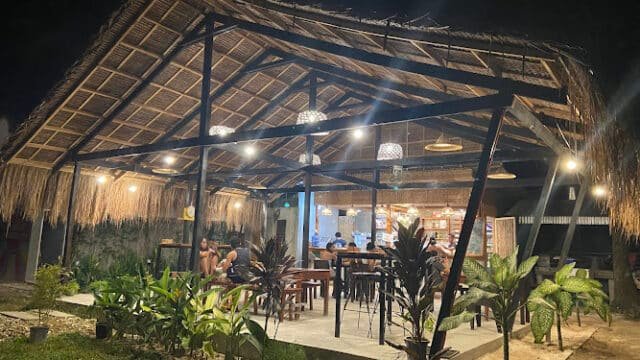 Outdoor cafe in Siargao with a thatched roof, wooden tables, hanging lights, and lush plants glowing at night.