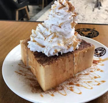 Thick Siargao toast topped with whipped cream and cinnamon, served on a white plate with a sweet caramel drizzle.