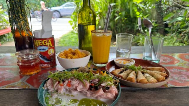 Outdoor table with plates of food, a drink, and a sardines can set against lush Siargao greenery in the background.