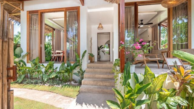 Modern tropical Siargao villa with large glass doors, lush green plants, and a small stone staircase at the entrance.