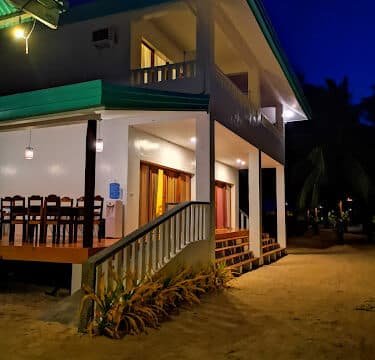 Two-story Siargao beach house with lit balcony and stairs, taken at night with warm indoor lights.