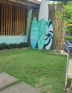Three surfboards stand on grass by a bamboo fence, near a building with a sign reading Tres Island Siargao in scenic Siargao.