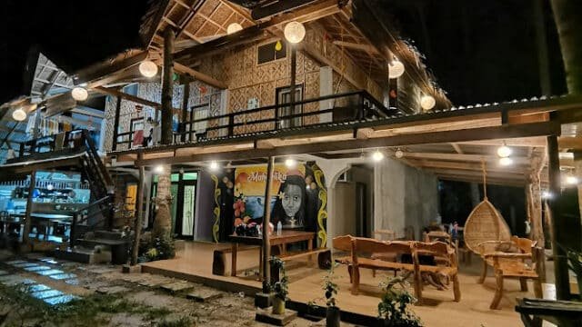 A cozy, well-lit two-story Siargao house with bamboo decor and hanging lanterns at night.
