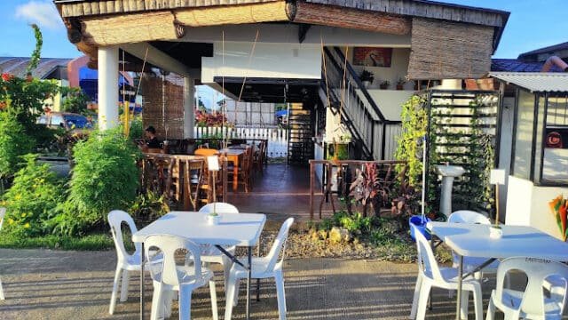Outdoor cafe in Siargao with white plastic tables, lush plants, and a wooden building beneath a clear blue sky.