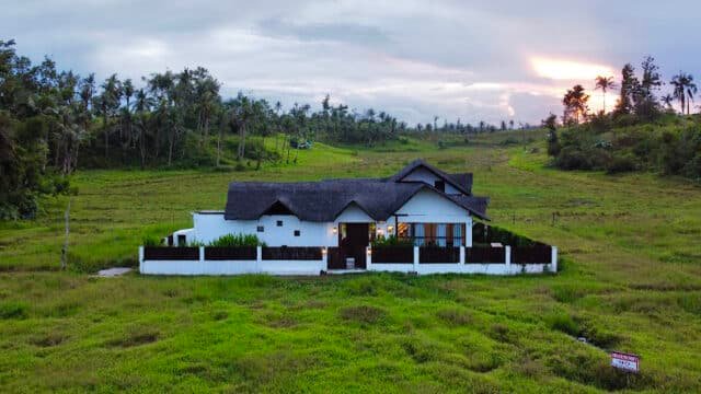 A white house with a dark roof sits in a large green field in Siargao under a cloudy sky at sunset.