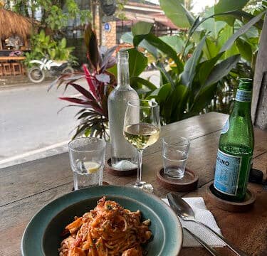 Plate of pasta, wine glass, water bottle, and glass on a wooden table with lush Siargao greenery in the background.